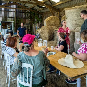 Groupe de visiteurs dégustant des produits fermiers lors d’une visite de bergerie, entourés de bottes de foin dans une ferme de l’Avesnois